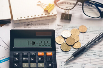 Conceptual tax 2025 symbol. word TAX 2025 on a calculator with documents on the desk. Income tax...