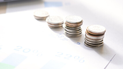 A stack of coins on top of a piece of paper with a graph. The coins are silver and gold and are piled on top of each other