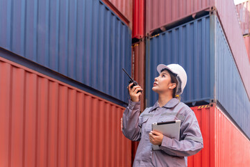 young asian female in safety gear and hard hat holding tablet computer,foreman working in shipping yard,control loading container box,communicate with walkie talkie