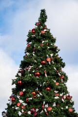 Large artificial Christmas tree decorated with classic red bulb ornaments and red and white candy shaped ornaments outdoors, celebrating the Christmas holiday season
