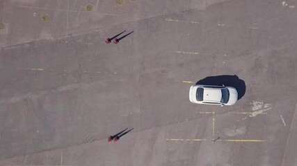 Aerial view of a white car on an empty asphalt lot surrounded by orange traffic cones in daylight