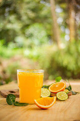 A glass of freshly squeezed orange juice on a wooden table surrounded by orange slices and orange leaves