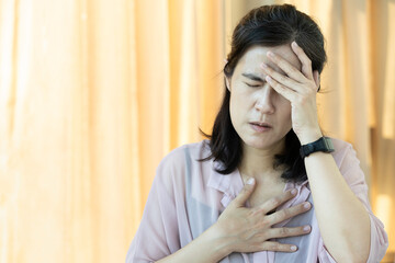 Asian woman experiencing symptoms of palpitations and dizziness,holding her chest,sensation of...