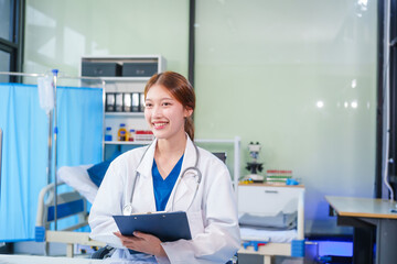 A young Asian female doctor, confidently dressed in a white uniform, sits at a computer desk in a hospital. She smiles while using a laptop, showcasing professionalism and dedication