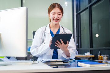 A young Asian female doctor, confidently dressed in a white uniform, sits at a computer desk in a...