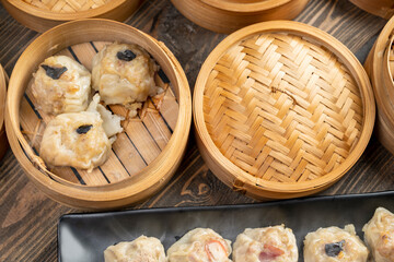 Assorted chinese dim sum dumpling on the plate with bamboo wooden basket bowl on wooden table
