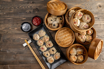 Assorted chinese dim sum dumpling on the plate with bamboo wooden basket bowl and chopstick with sauce on wooden table
