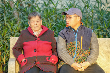On a cold winter evening, a Chinese woman in her 70s and her grandson, a man in his 30s, sit on a...