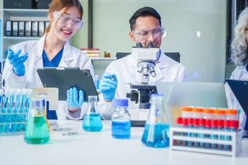 Two Asian men and women sit at a table in a laboratory, conducting research on liquids. They use...