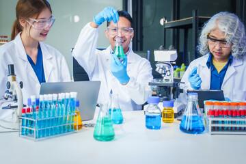 Two Asian men and women sit at a table in a laboratory, conducting research on liquids. They use microscopes, petri dishes, and test tubes filled with various chemicals for analysis