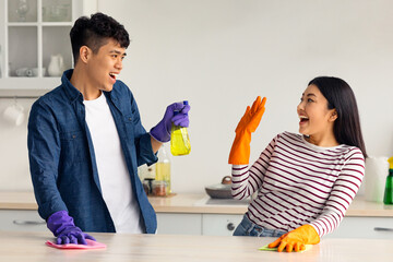 Joyful asian lovers young man and woman in casual clothes having fun while cleaning kitchen...
