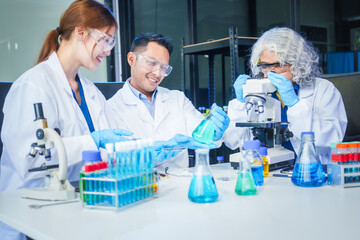 Two Asian men and women sit at a table in a laboratory, conducting research on liquids. They use microscopes, petri dishes, and test tubes filled with various chemicals for analysis