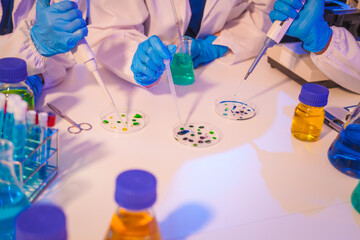 Two Asian men and women sit at a table in a laboratory, conducting research on liquids. They use microscopes, petri dishes, and test tubes filled with various chemicals for analysis