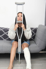 A 30-year-old brunette Latina woman tries to get up with difficulty from the chair with a crutch...