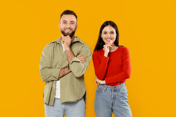 A young couple stands side by side in a vibrant yellow setting. They share playful expressions while resting their chins on their hands, showcasing their affection and joy.