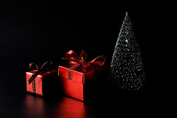 Miniature Christmas tree with red present boxes on black background.