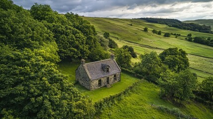 Serene Aerial View of an Isolated Stone Cottage Surrounded by Lush Green Hills and Trees Under a Dramatic Sky in the Countryside Landscape