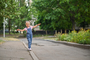 Fototapeta premium The girl walks along the curb, balancing with her arms outstretched