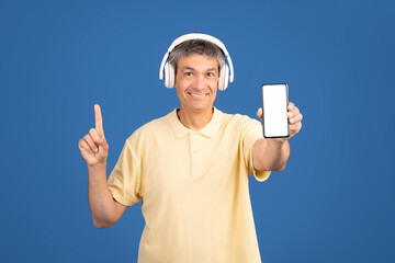 A middle aged man in his 50s is smiling and pointing with one finger while holding a smartphone in...