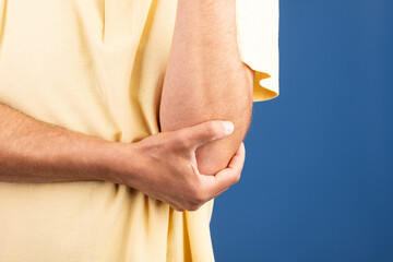 A mature Caucasian man in his 50s is sitting alone, looking uncomfortable as he holds his elbow....