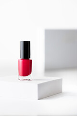 Red nail polish bottle with black tap on the podium on white isolated background , beauty and make ads