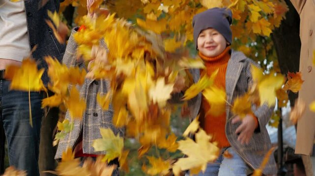 Parents witness daughter with son tossing autumn leaves into air. Parents with preschooler children create delightful moments by throwing golden leaves. Parents share autumn joy with daughter and son