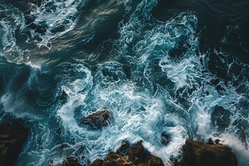 Fototapeta premium Strong waves tumble over rugged rocks along the coastline, creating a dynamic display of white foam against deep blue water, illustrating nature's power and beauty.