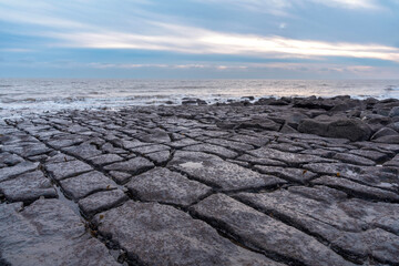 Rocky coastal landscape at twilight with textured stone formations and rhythmic ocean waves