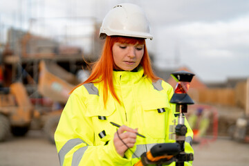 Woman construction worker with bright orange hair records data at a job site during overcast weather