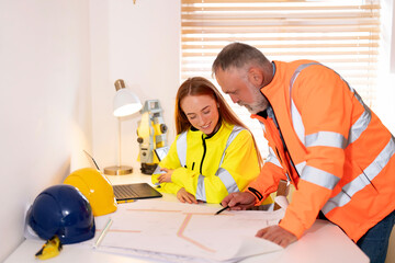 Workers collaborate on construction project plans in a bright office with safety gear