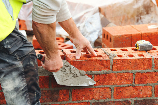 Skilled builder bricklayer laying bricks with precision at a construction site in the afternoon sun