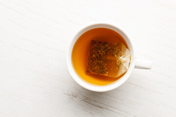 Cup of hot tea blended from rooibos, spearmint, apple, baobab on white wooden table.