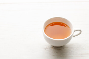Cup of hot tea blended from rooibos, spearmint, apple, baobab on white wooden table.