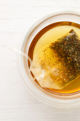 Cup of hot tea blended from rooibos, spearmint, apple, baobab on white wooden table.