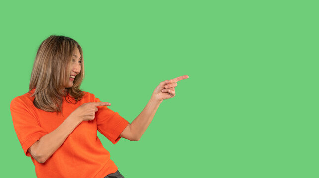 Woman in orange shirt gesturing pointing and smiling against a bright green background