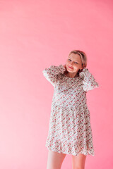 Beautiful blonde woman in summer dress smiling on pink background