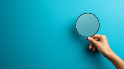 hand holding round mirror against blue background, reflecting light