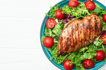 Grilled chicken breast ( fillet ) with lattuce salad and cherry tomatoes . Top view