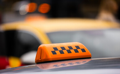 Yellow taxi with an orange light top at a busy city street during the day. Brightly colored taxi with an orange topped light is parked near other taxis in a bustling urban environment.