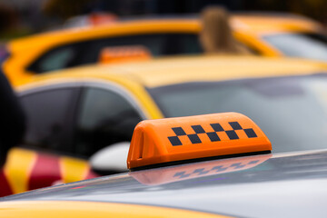 Yellow taxi cabs lined up at a busy city street during the day. Bright yellow taxi cabs wait in line on a bustling city street. Passersby go about their day, showcasing urban life and transportation.