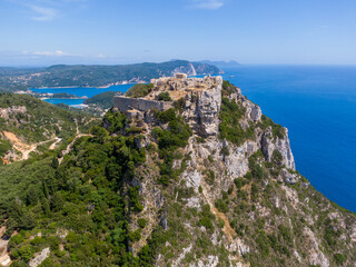 A breathtaking aerial view of Angelokastro, a Byzantine castle perched atop a cliff on the Greek island of Corfu. The ruins stand in stark contrast to the vibrant blue sea and green landscape,