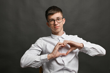 A smiling young man with glasses wearing white t shirt doing heart symbol shape with hands. romantic love concept.. 