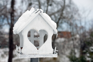 Naklejka premium Wooden bird feeder. for feed and wheat inside. birdhouse on a blurred background of outdoors. feeders in the autumn park. winter season. bird care. close-up. cold weather. winter time. environment