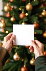Vertical Mock up: man's hands holding a blank card against the background of a festive Christmas tree decorated with balls in gold and mocha mousse. Trendy mocha mousse color. Empty space for text. Ne