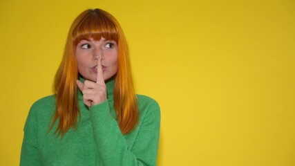 Woman with orange hair and green sweater holding finger to lips in shush gesture against a bright yellow background