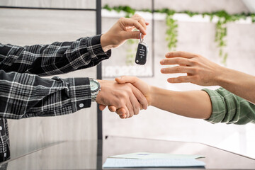 Two businessmen shaking hands after signing a car sale contract, with car keys being delivered