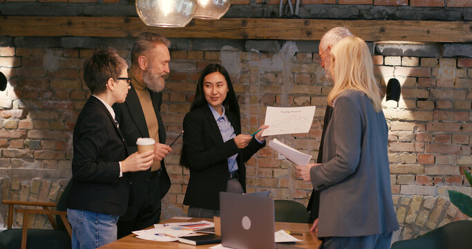 Young Asian woman points to financial chart during meeting