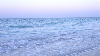 White-tipped waves move gracefully over sand, sky painted in gentle pre-dawn colors, forming peaceful coastal scene exuding early morning tranquility. Ocean serenity concept.