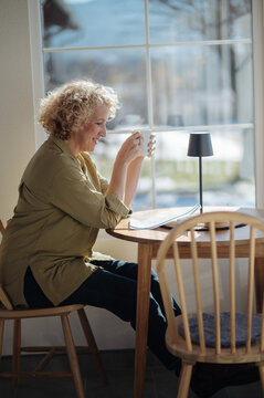 Woman drinking coffee and sit at home holding paper read.