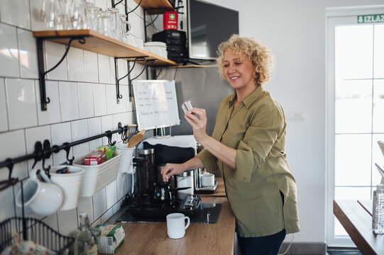 Smiling middle-aged woman making coffee in the kitchen.